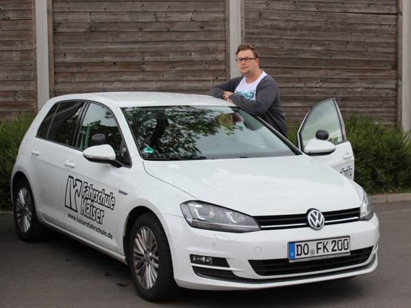 Weißer VW Golf VII blue TDI der Fahrschule Kaiser mit Logo an der Seite und geöffneter Fahrertür, Kennzeichen DO FK 200; daneben steht ein Mann