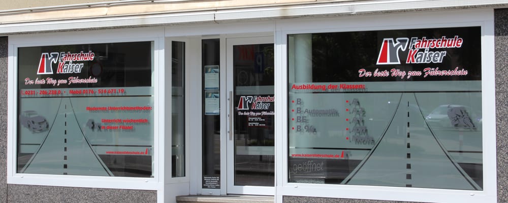 Ein weiteres Filial-Schaufenster mit derselben Logo-Beklebung, daneben eine aufgeklebte Fahrbahn mit Mittelstreifen und die Liste der ausgebildeten Klassen