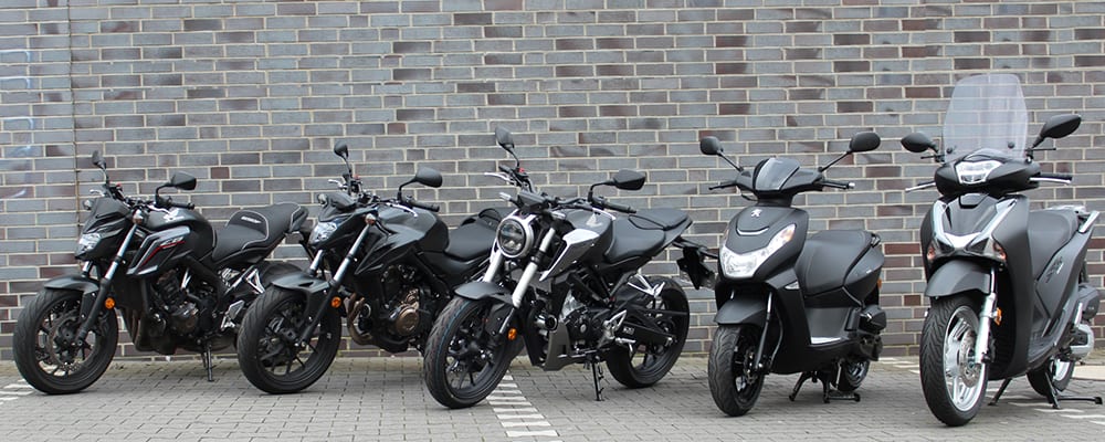Fünf schwarze Fahrzeuge der Fahrschule Kaiser nebeneinander vor einer Klinkerwand: drei Honda-Motorräder, ein Peugeot-Roller und ein Honda-Roller mit Windschutzscheibe